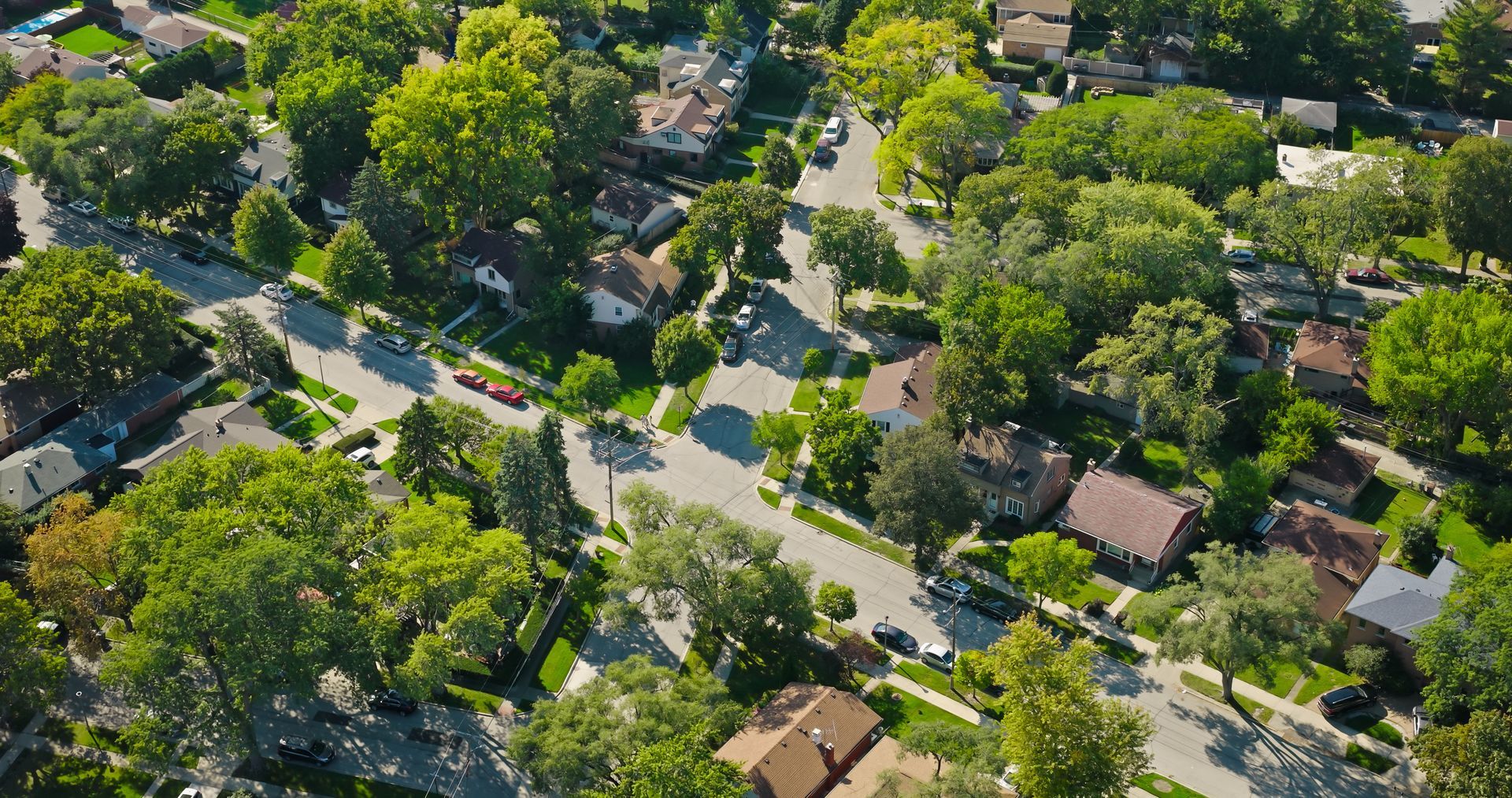 Aerial view of a residential neighborhood with houses, streets, and lush green trees. Sunny day. Aerial view of a residential neighborhood with houses, streets, and lush green trees. Sunny day.