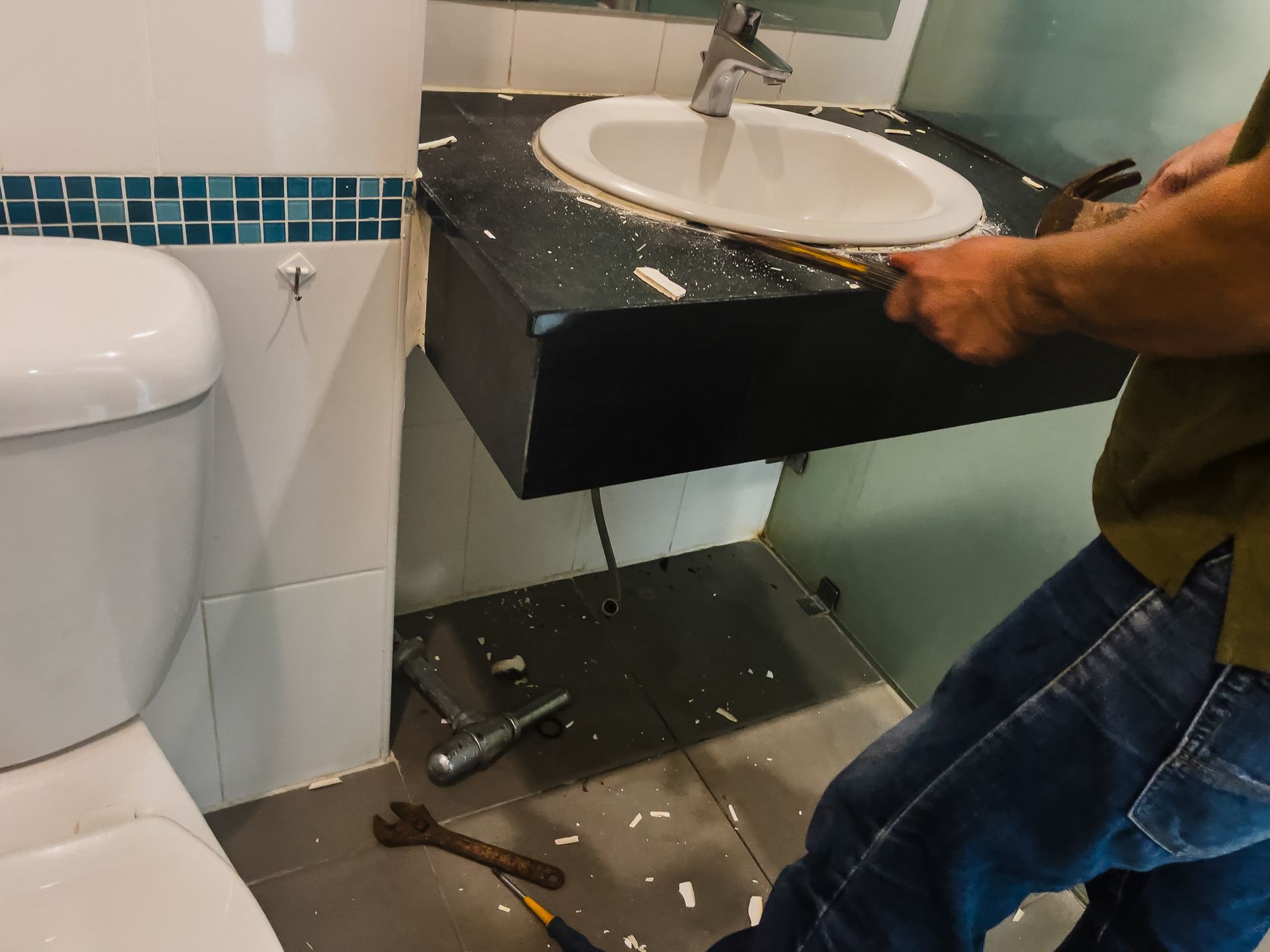 Person removing a bathroom sink from the wall with tools. The sink is white, and the countertop is black. Person removing a bathroom sink from the wall with tools. The sink is white, and the countertop is black.