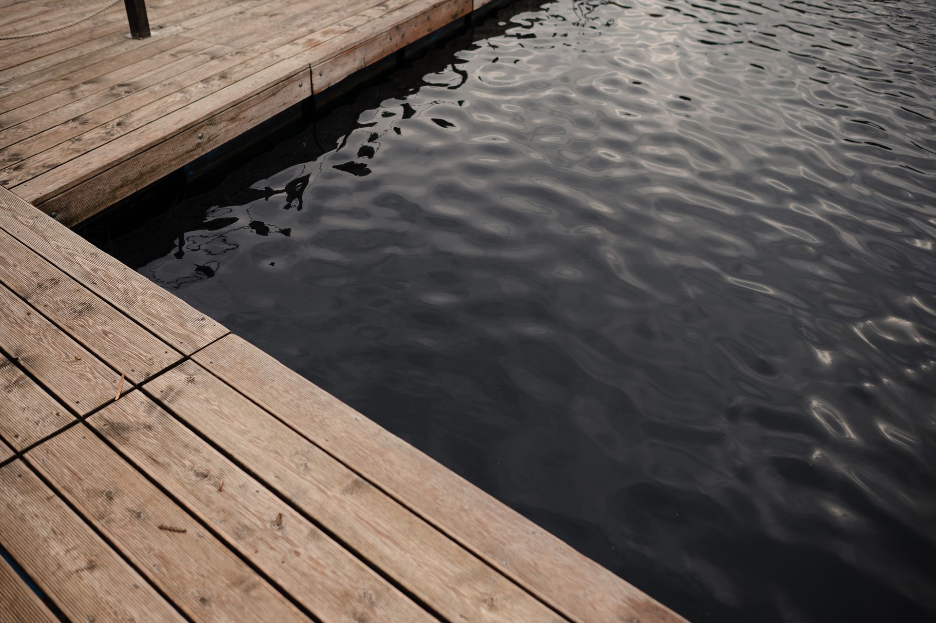 Wooden dock edge bordering dark, rippled water. Wooden dock edge bordering dark, rippled water.
