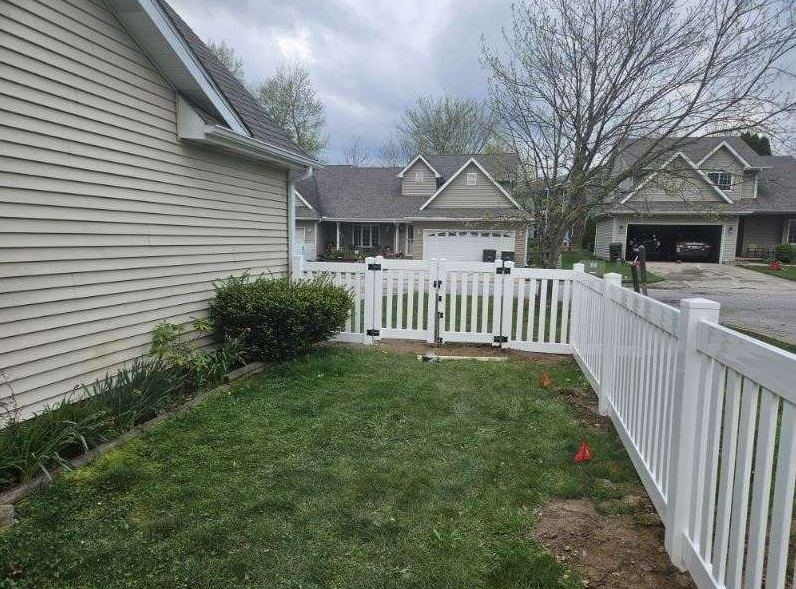 Person using a power drill on a wooden fence outdoors, near a chain link fence. Person using a power drill on a wooden fence outdoors, near a chain link fence.