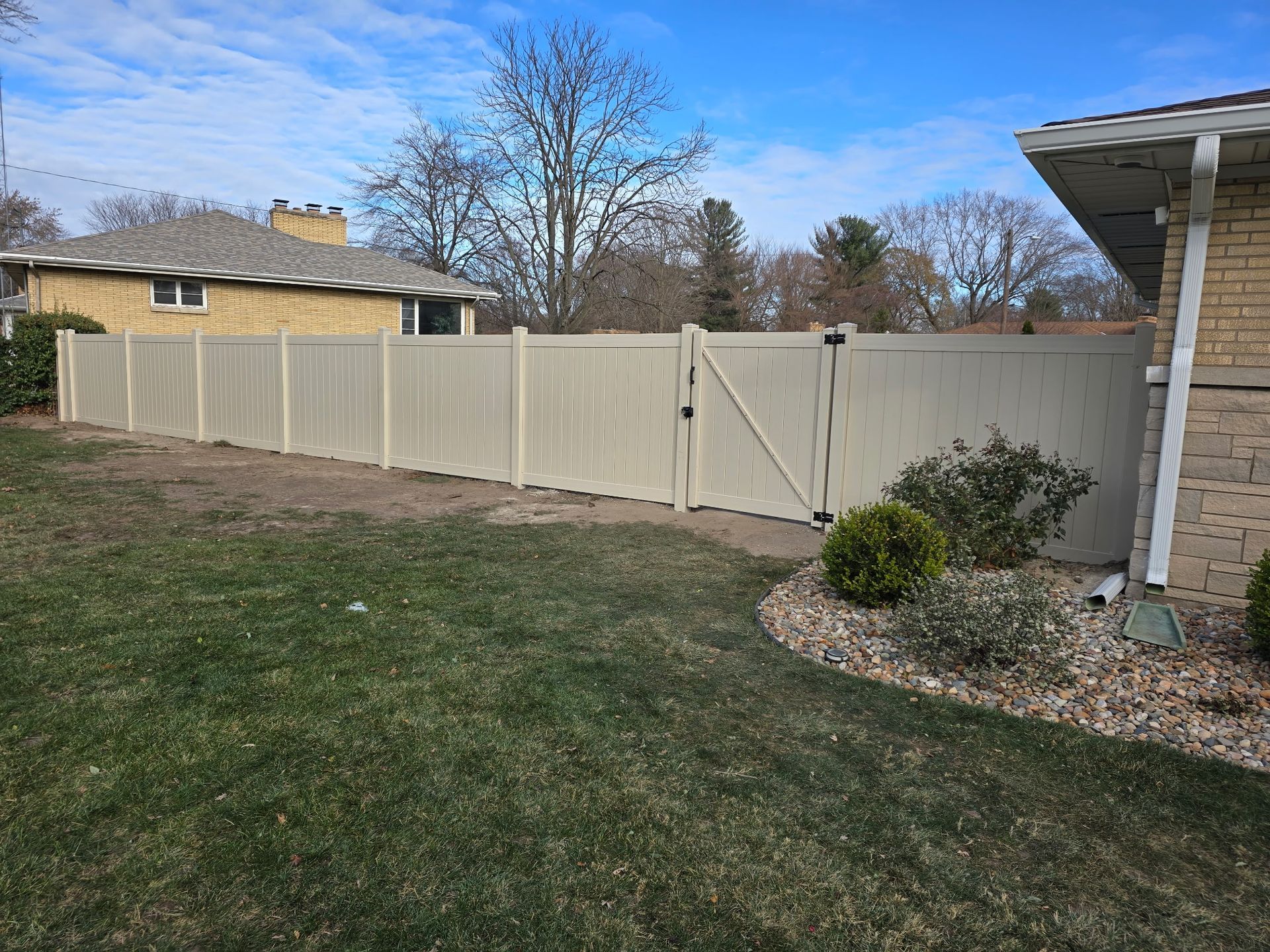 Beige vinyl fence with gate in residential yard, next to brick home.
