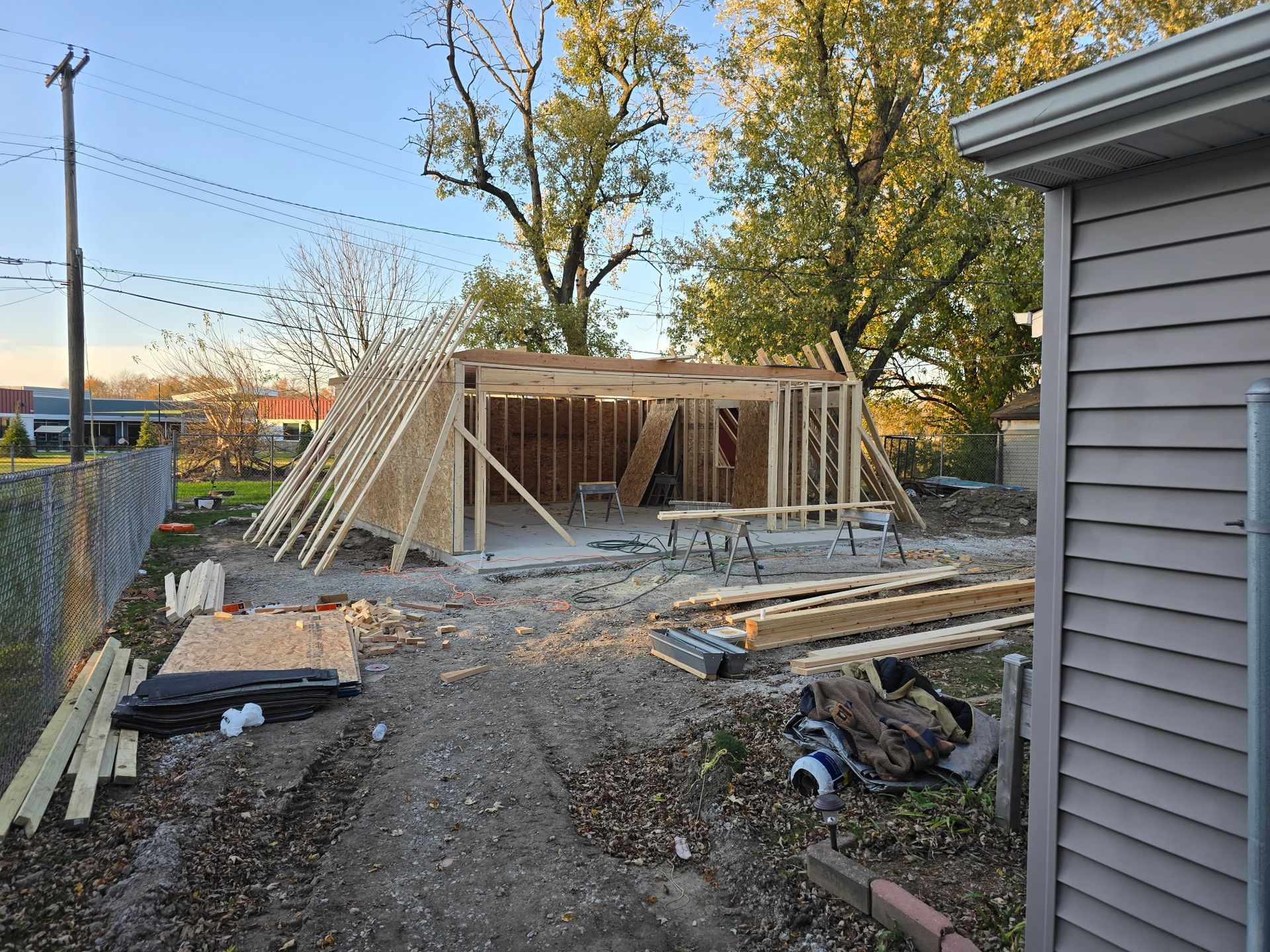 Framing of a wooden structure in a yard, under construction, with materials and tools present.