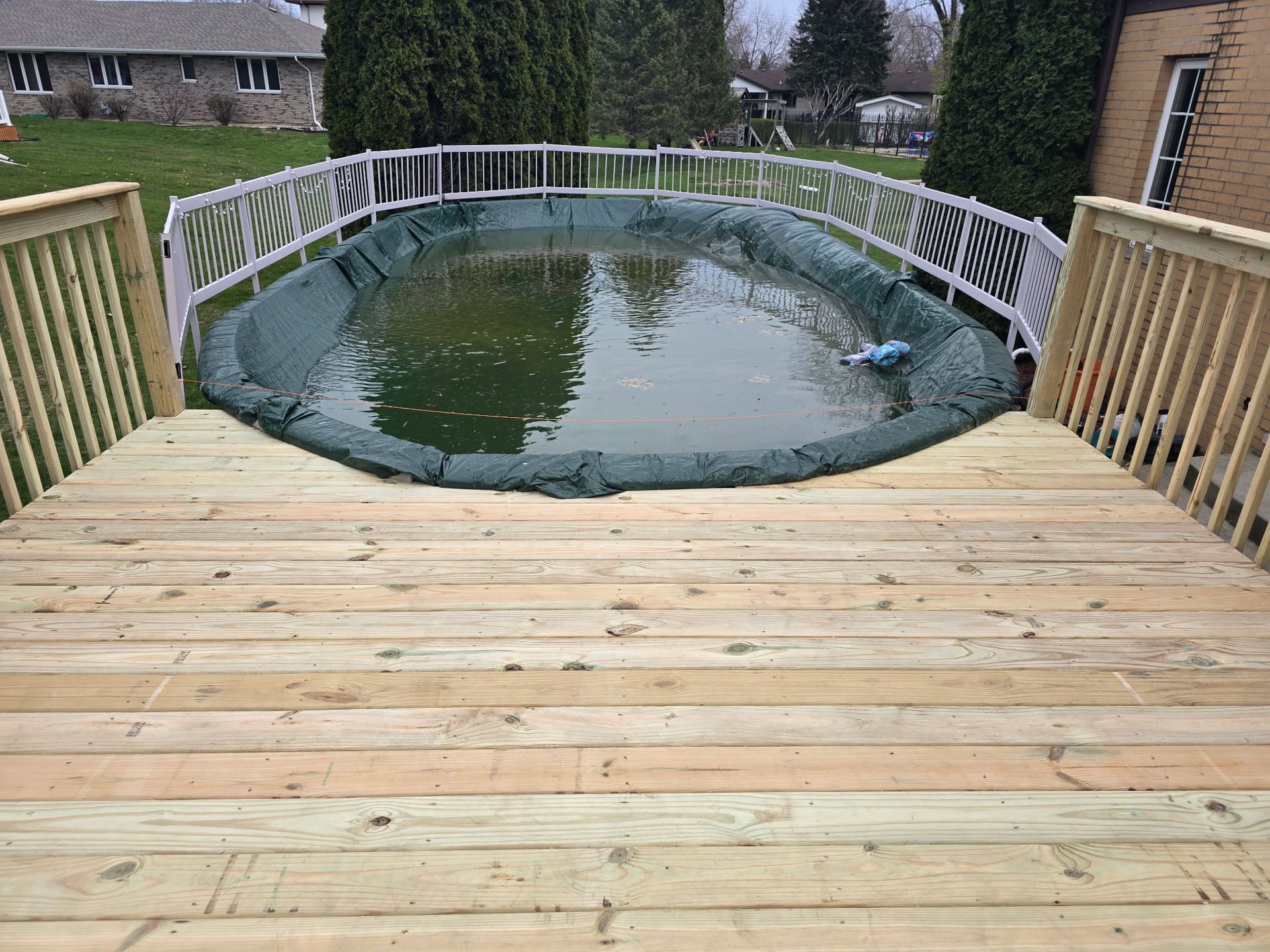 Wooden deck overlooking an above-ground pool covered with a green tarp.