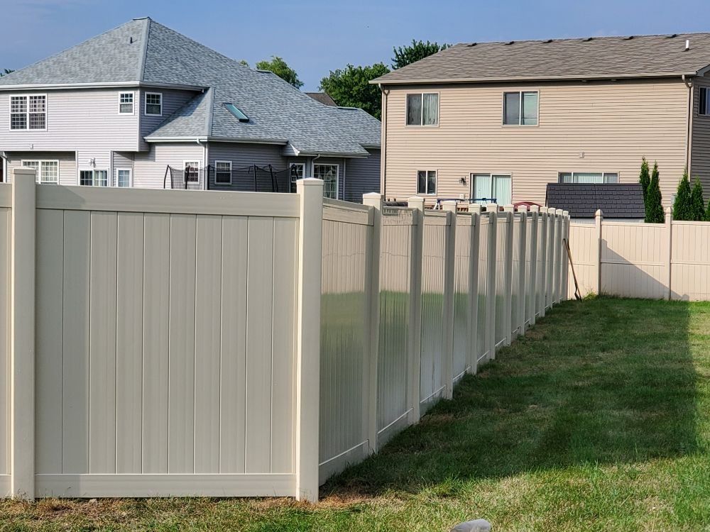 Tan vinyl fence in a backyard setting with houses in the background. Tan vinyl fence in a backyard setting with houses in the background.