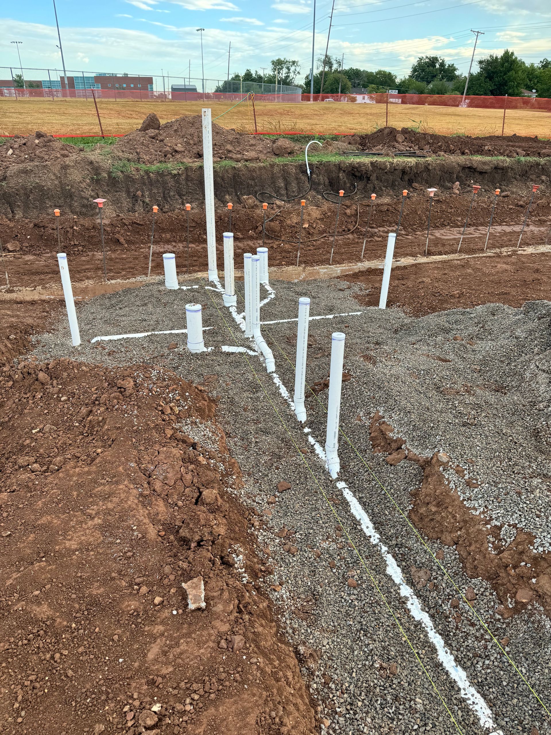 Cowboys Plumbing - Pipes installed in a gravel trench on a construction site. Dirt surrounds the trench.