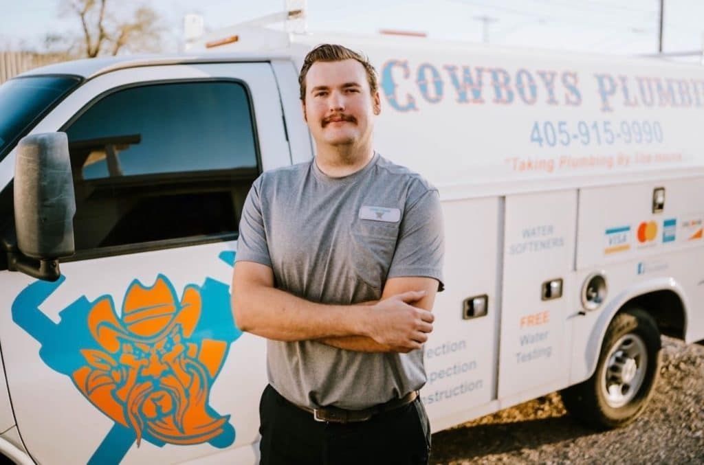 Man with crossed arms stands in front of a white plumbing van with the business name