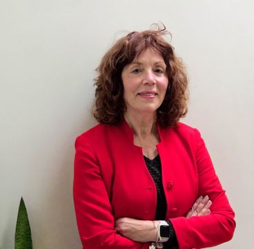 Woman in a red blazer stands with arms crossed against a plain wall.