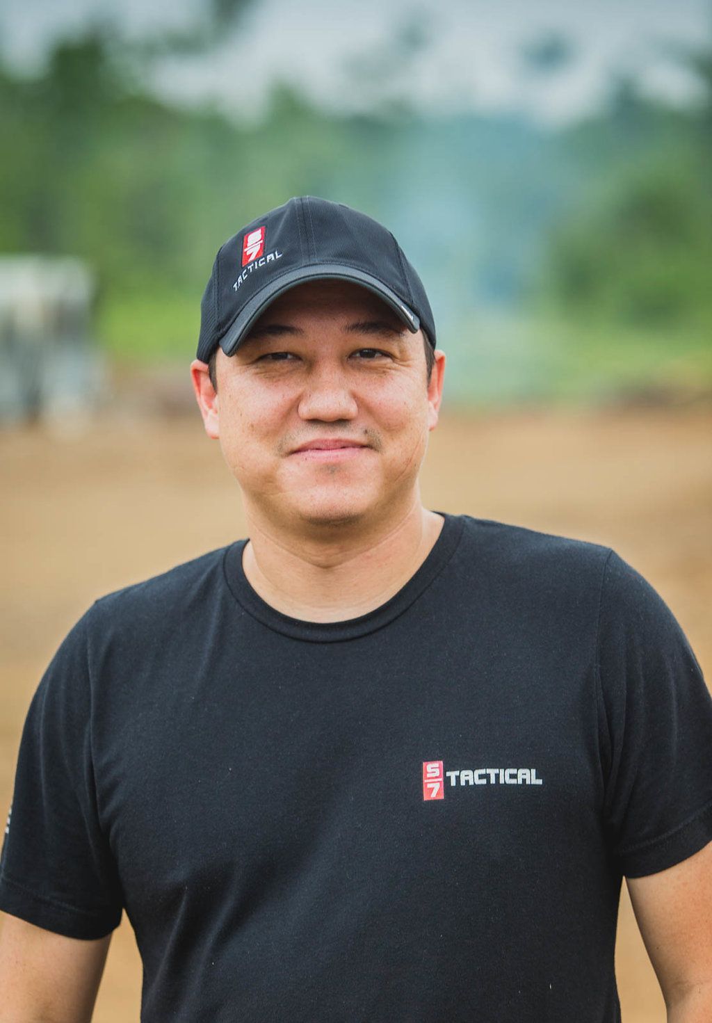 A man wearing a black t-shirt and a hat is standing in a field.