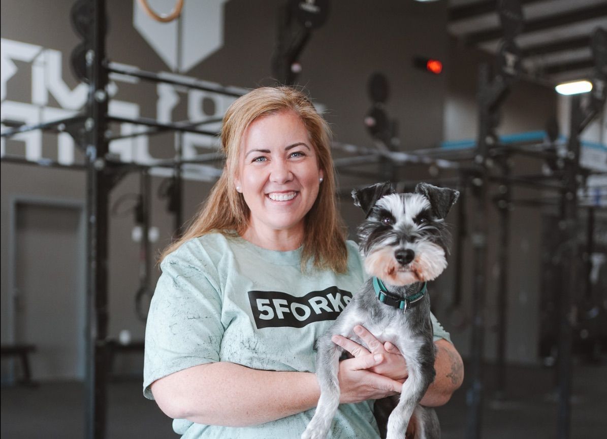 A woman is holding a small dog in her arms in a gym.