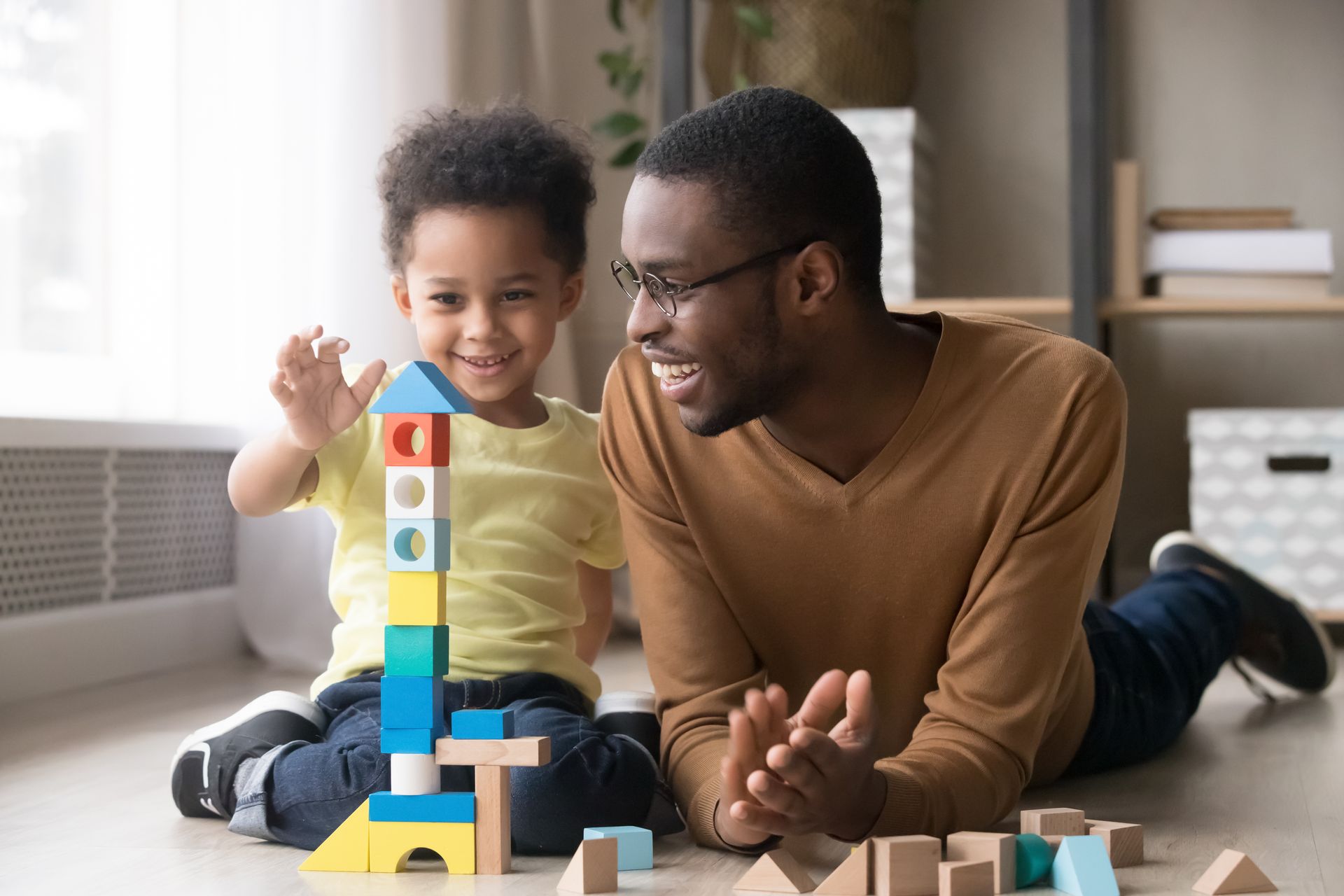 A man and a child are playing with wooden blocks on the floor.