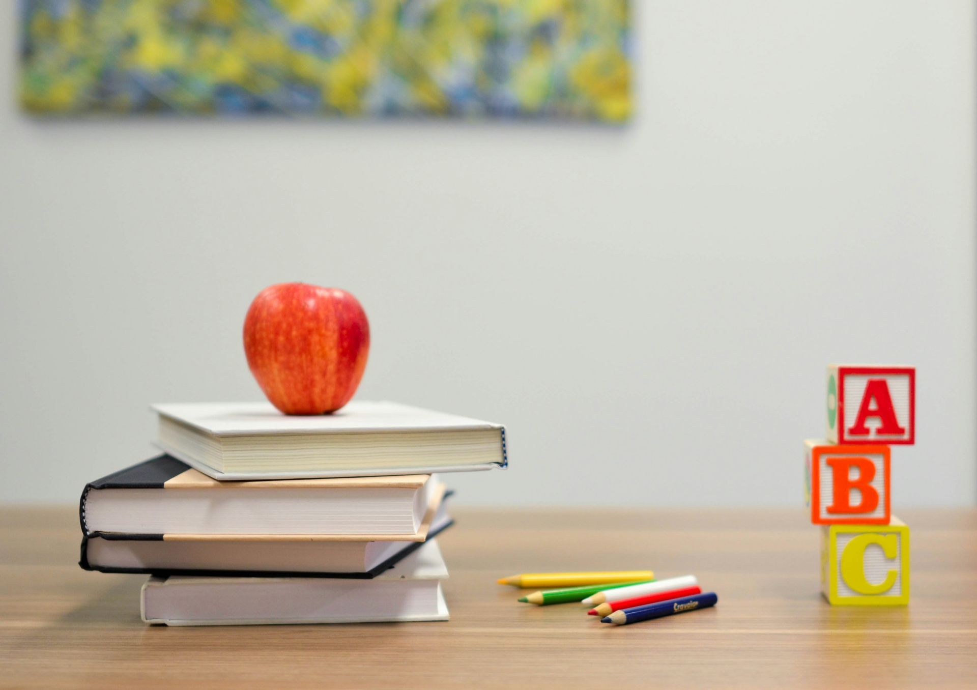 An apple is sitting on top of a stack of books on a table.