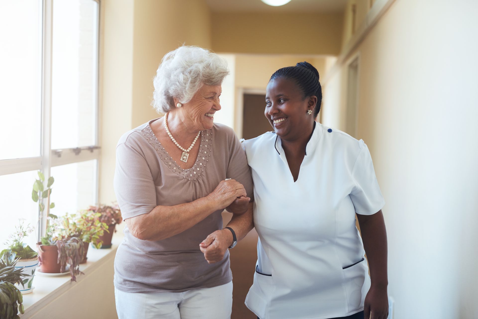 A smiling home caregiver and an elderly woman walk together, smiling.