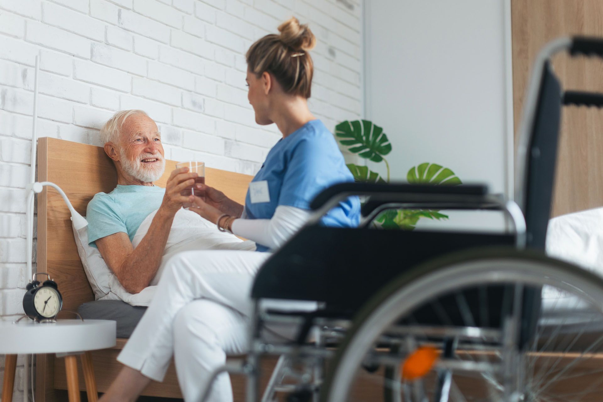Home after surgery caregiver assisting senior man drinking water in bed for recovery.