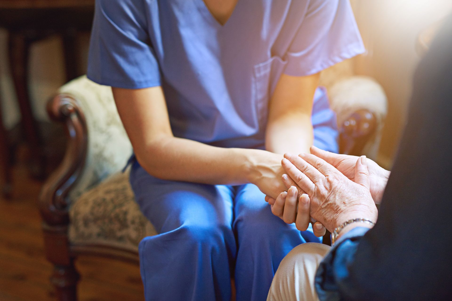 Caregiver holding an elderly person’s hand in a warm living room scene