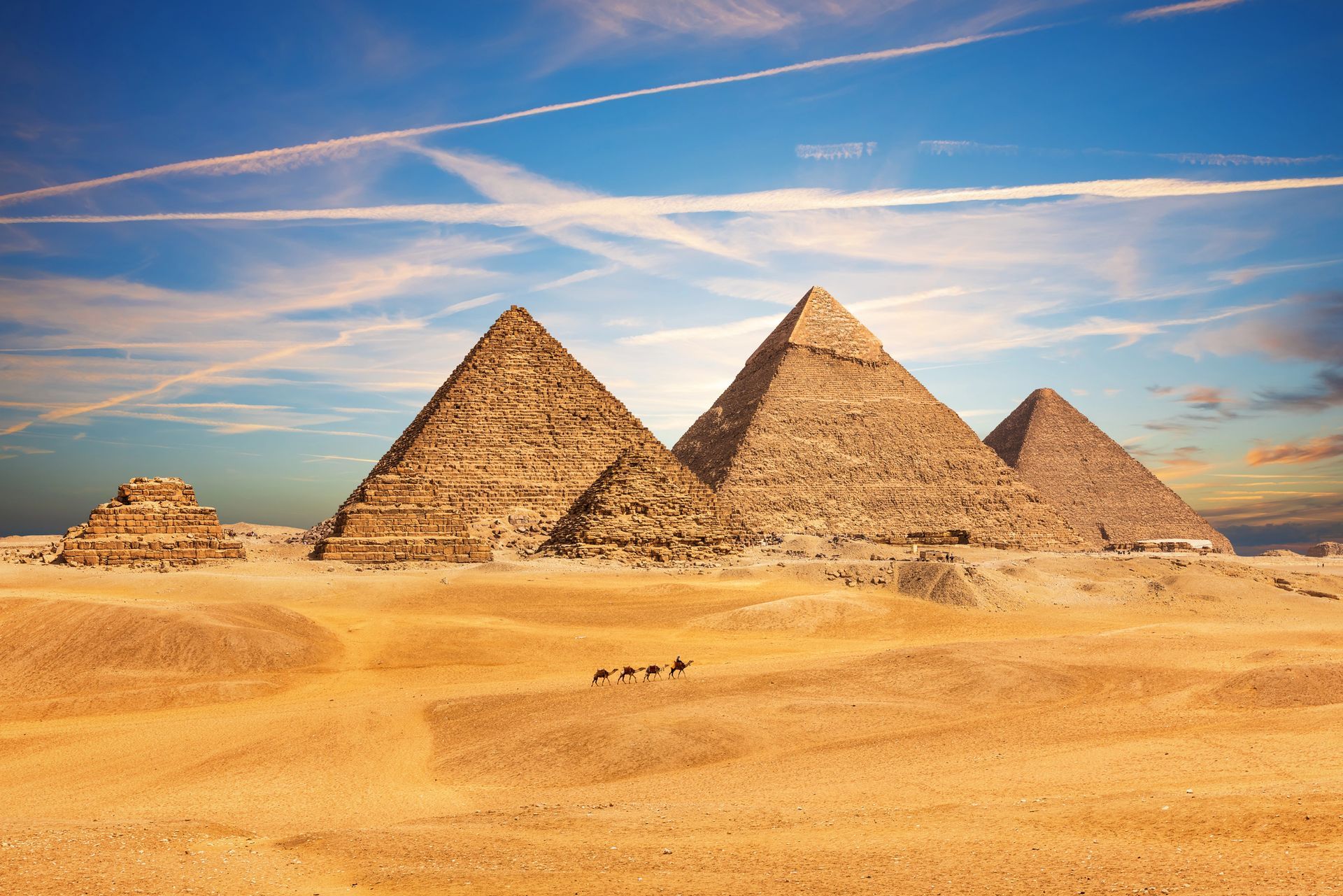Las pirámides de Giza se alzan desde un desierto dorado bajo un cielo azul con nubes tenues.