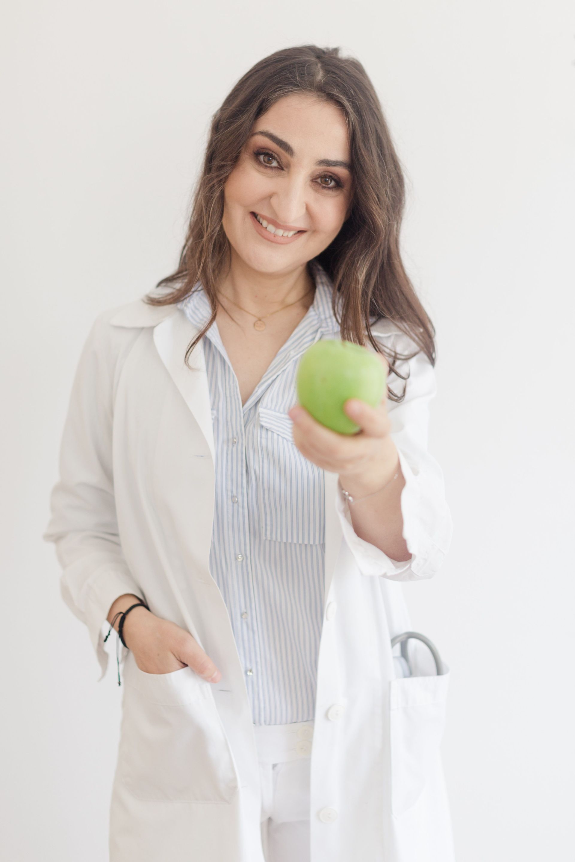 Smiling doctor in a white coat holding a green apple and a white reusable bag