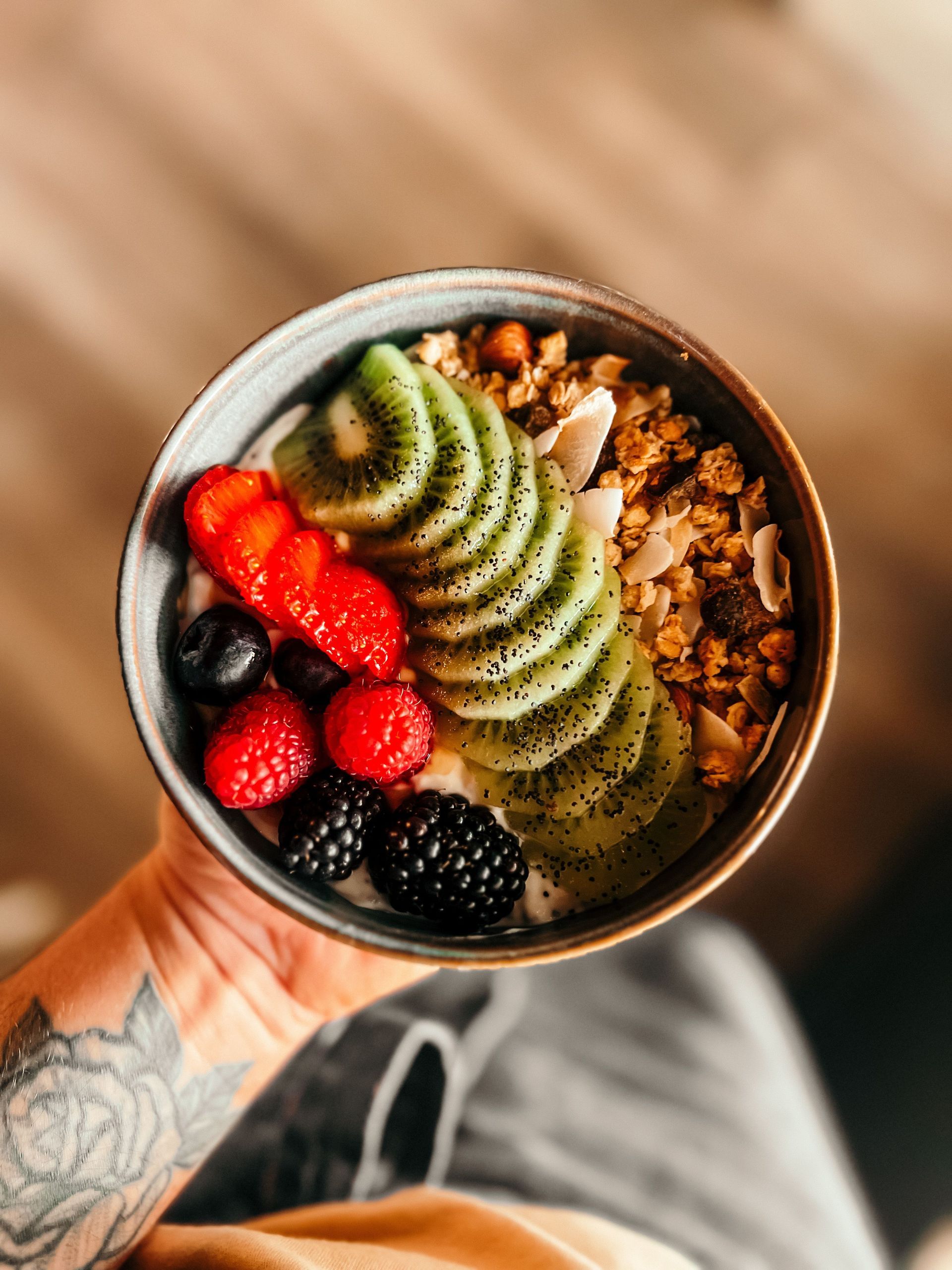 Hand holding a bowl of sliced kiwi, strawberries, blackberries, and granola