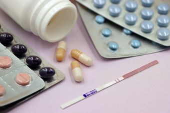 Pill bottles, loose tablets, blister packs, and a pregnancy test on a pink surface
