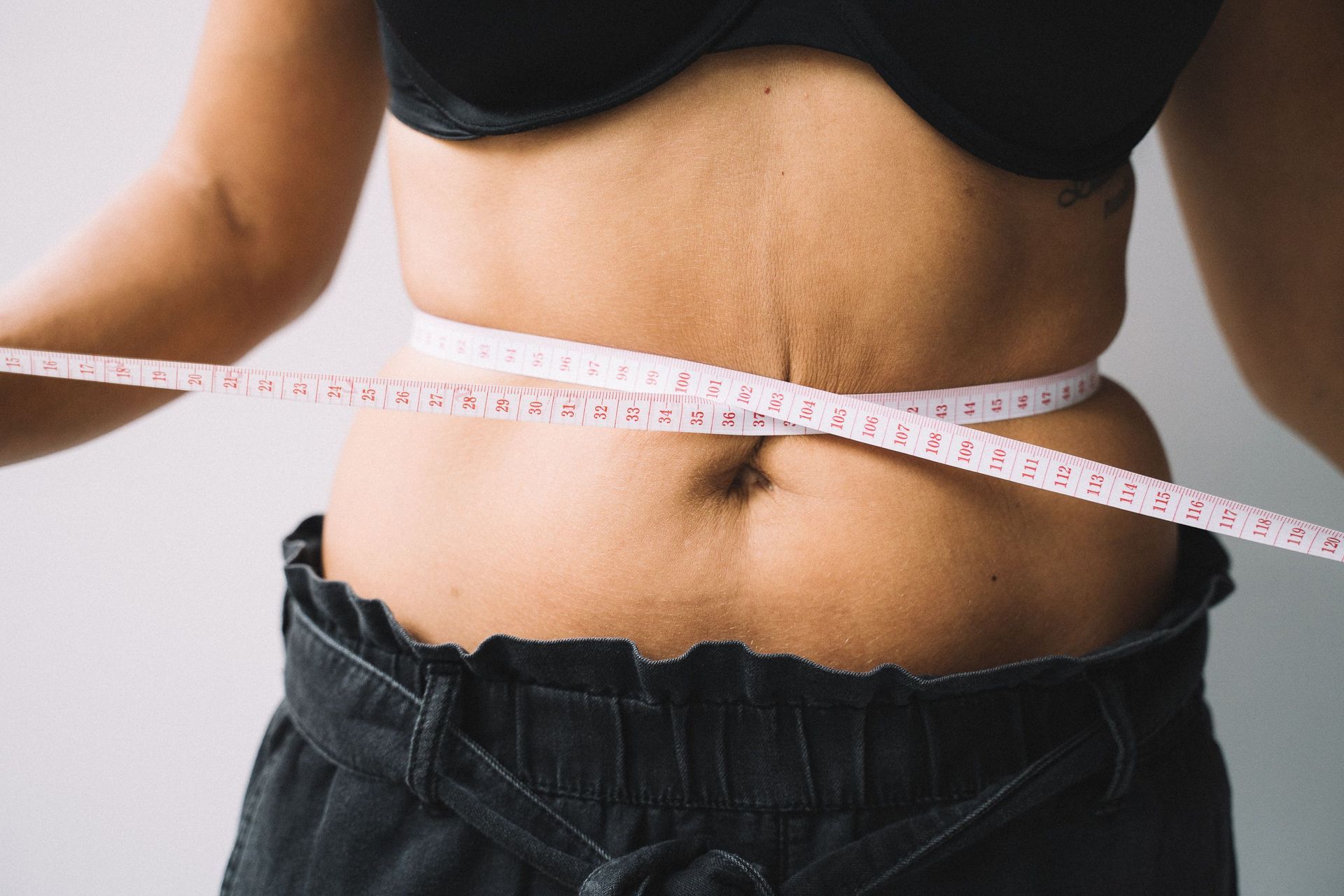 Person measuring waist with a pink tape measure over black clothing