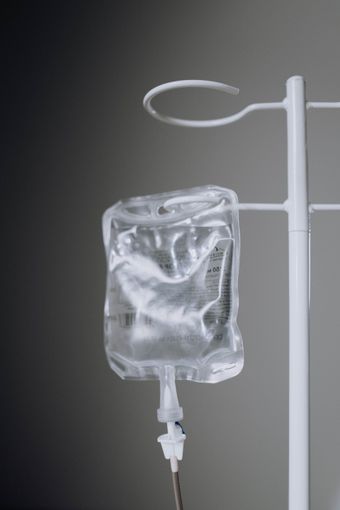 IV saline bag hanging on a metal stand, partially filled, against a gray background