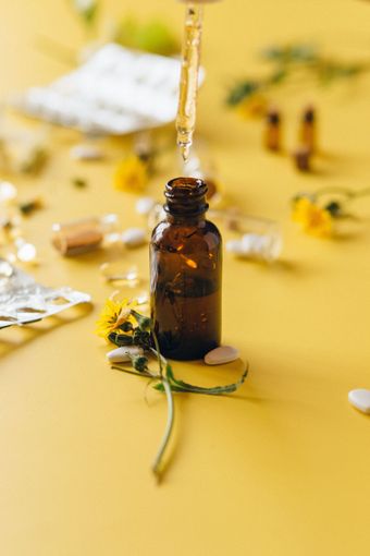 Amber dropper bottle with herbs and yellow flowers on a yellow surface