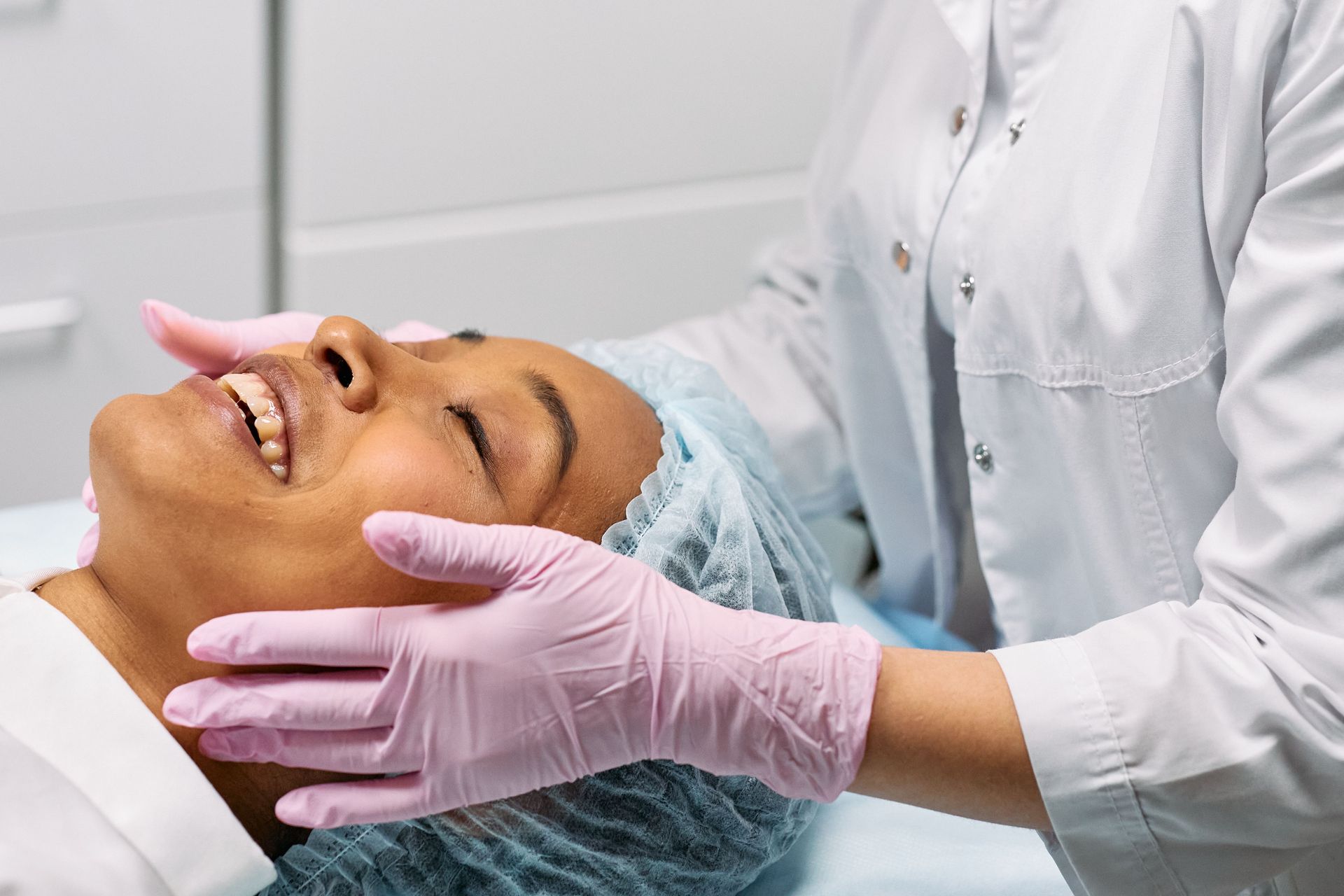 Gloved esthetician holding a client’s face during a facial treatment in a spa setting
