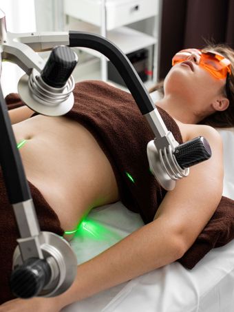Person receiving a spa treatment with a facial mask, orange goggles, and a device on the abdomen