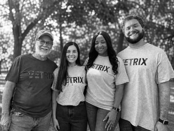Four people in gray Vetrix shirts standing together outdoors, smiling at the camera.