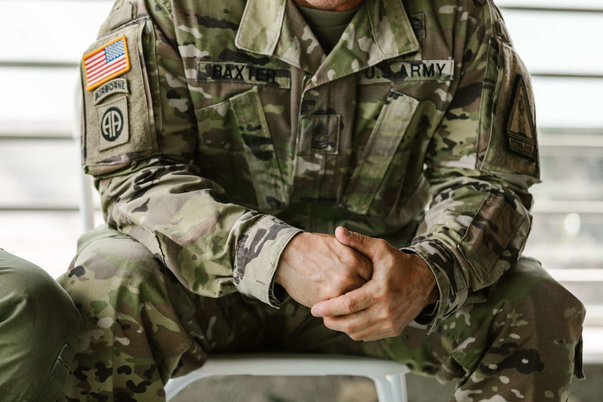 Soldier in camouflage uniform seated with hands clasped, showing a U.S. flag patch and name tag