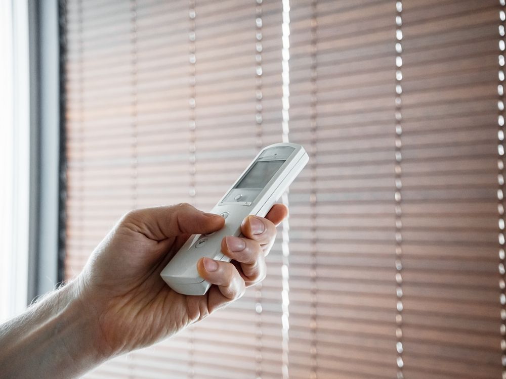 Hand Holding a White Remote Control, Adjusting Wooden Blinds — Wares Blinds, Screens & Awnings In Tannum Sands, QLD