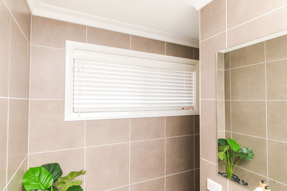 Bathroom with beige tiled walls, white window blinds, and a large mirror.