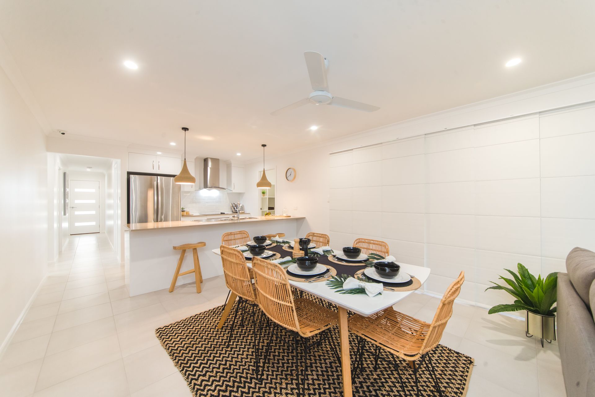 Dining area with table set for six, open to a kitchen. Beige wicker chairs, neutral decor.
