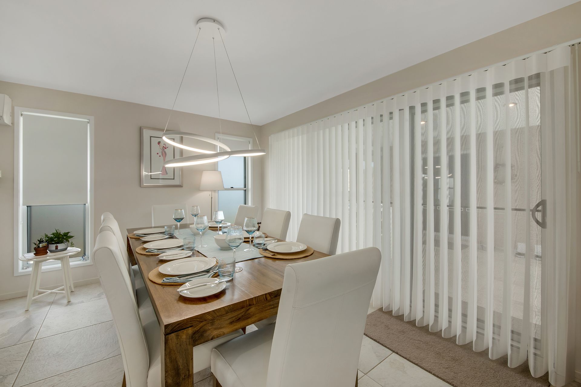 Dining room with wooden table, white chairs, and sheer vertical blinds.
