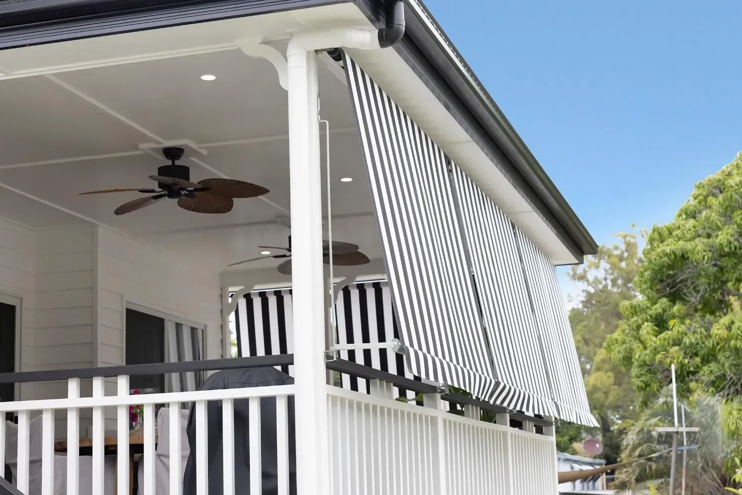 Black and White Striped Awning Shading a White Veranda, Next to Foliage, Under a Blue Sky — Wares Blinds, Screens & Awnings In Boyne Island, QLD