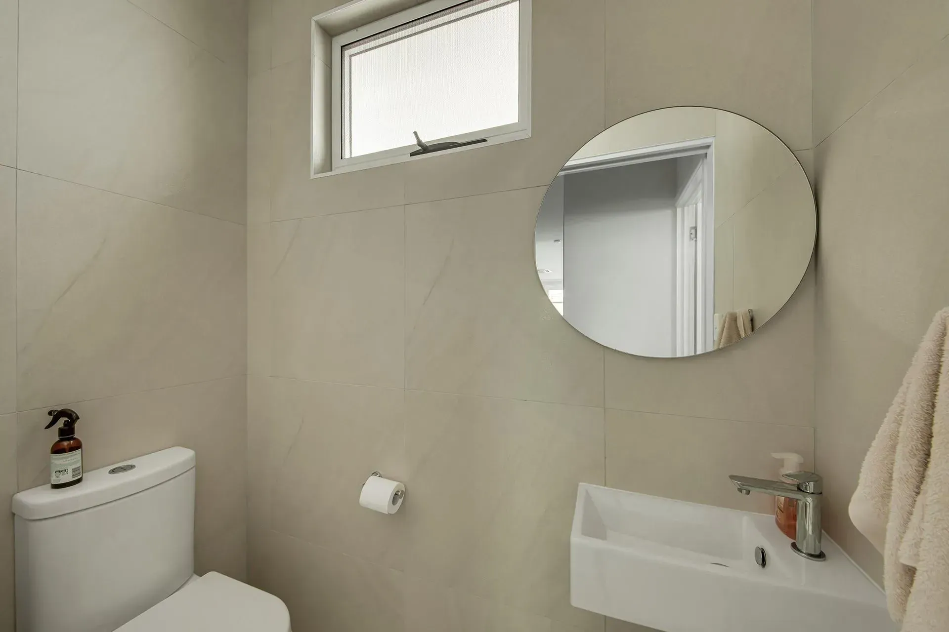 Small Modern Bathroom with A Toilet, Sink, Round Mirror, and Towel. Beige Walls — Wares Blinds, Screens & Awnings In Agnes Water, QLD