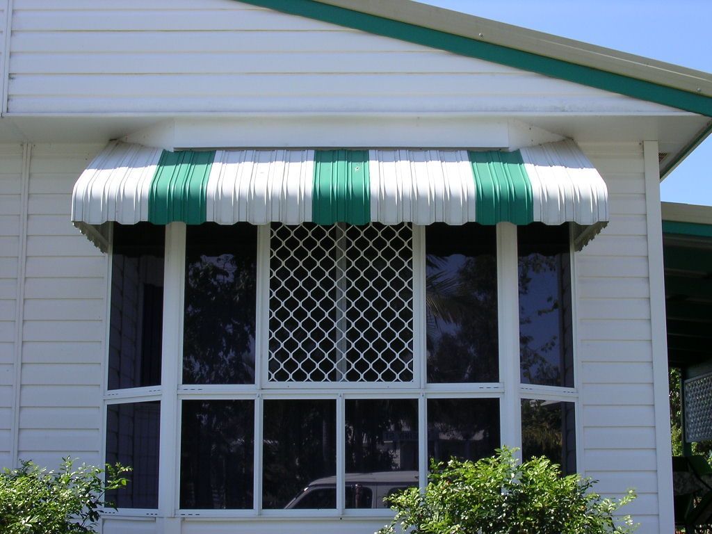 White house with a bay window covered by a green and white striped awning and security screens Wares Blinds, Screens & Awnings In Gladstone Central, QLD