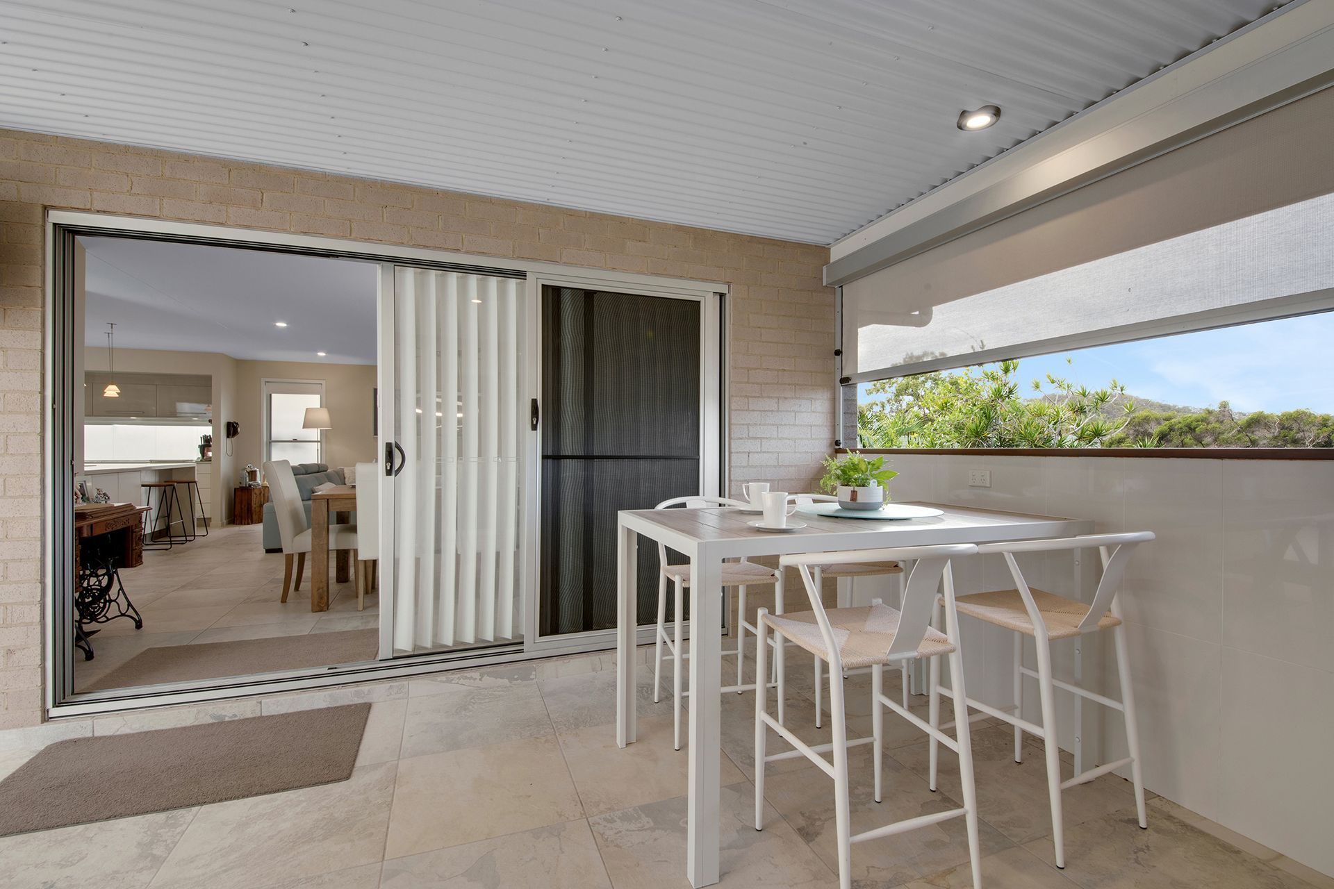 Outdoor patio with a white table and chairs, connected to an indoor dining area with a sliding door.