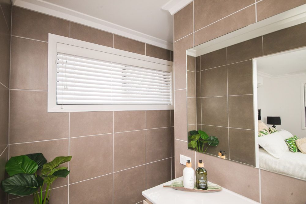 Bathroom with brown tiled walls, white trim, blinds, mirror, and decorative plants Wares Blinds, Screens & Awnings In Gladstone Central, QLD