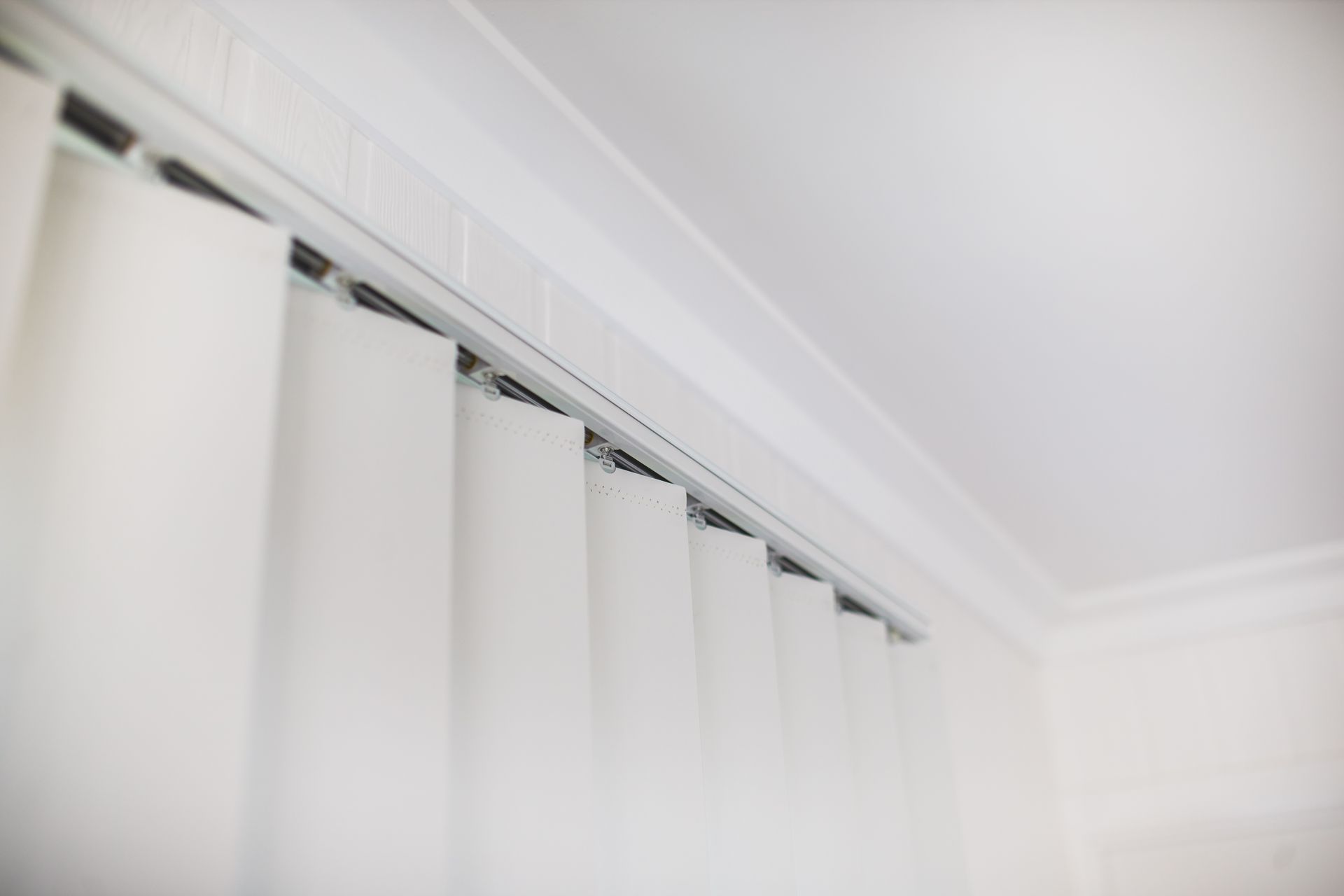 White Vertical Blinds Attached to The Ceiling, Partially Closed, in A Brightly Lit Room — Wares Blinds, Screens & Awnings In Yeppoon, QLD