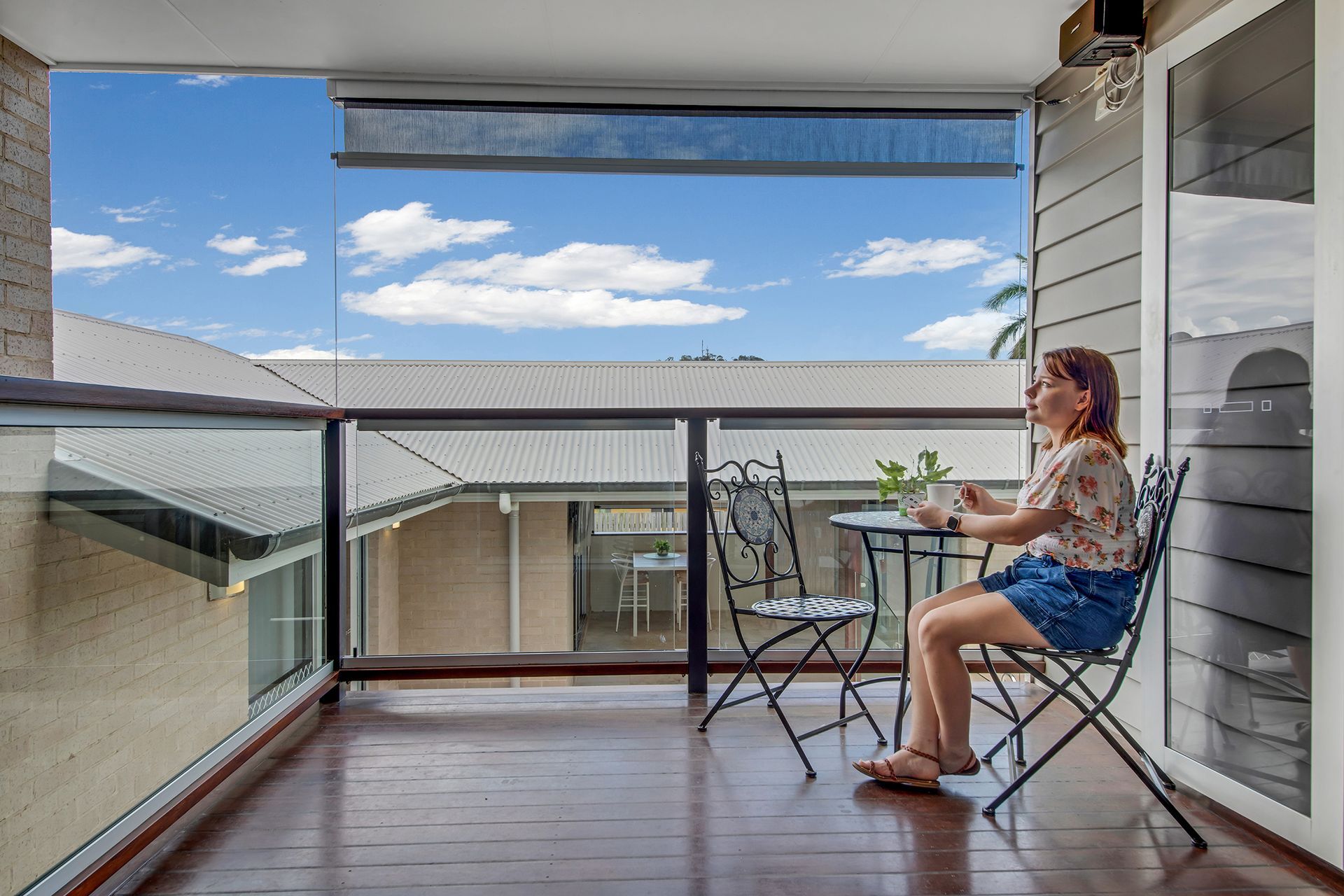 Woman Sits at Table on A Balcony, Overlooking a Clear Blue Sky — Wares Blinds, Screens & Awnings In Yeppoon, QLD