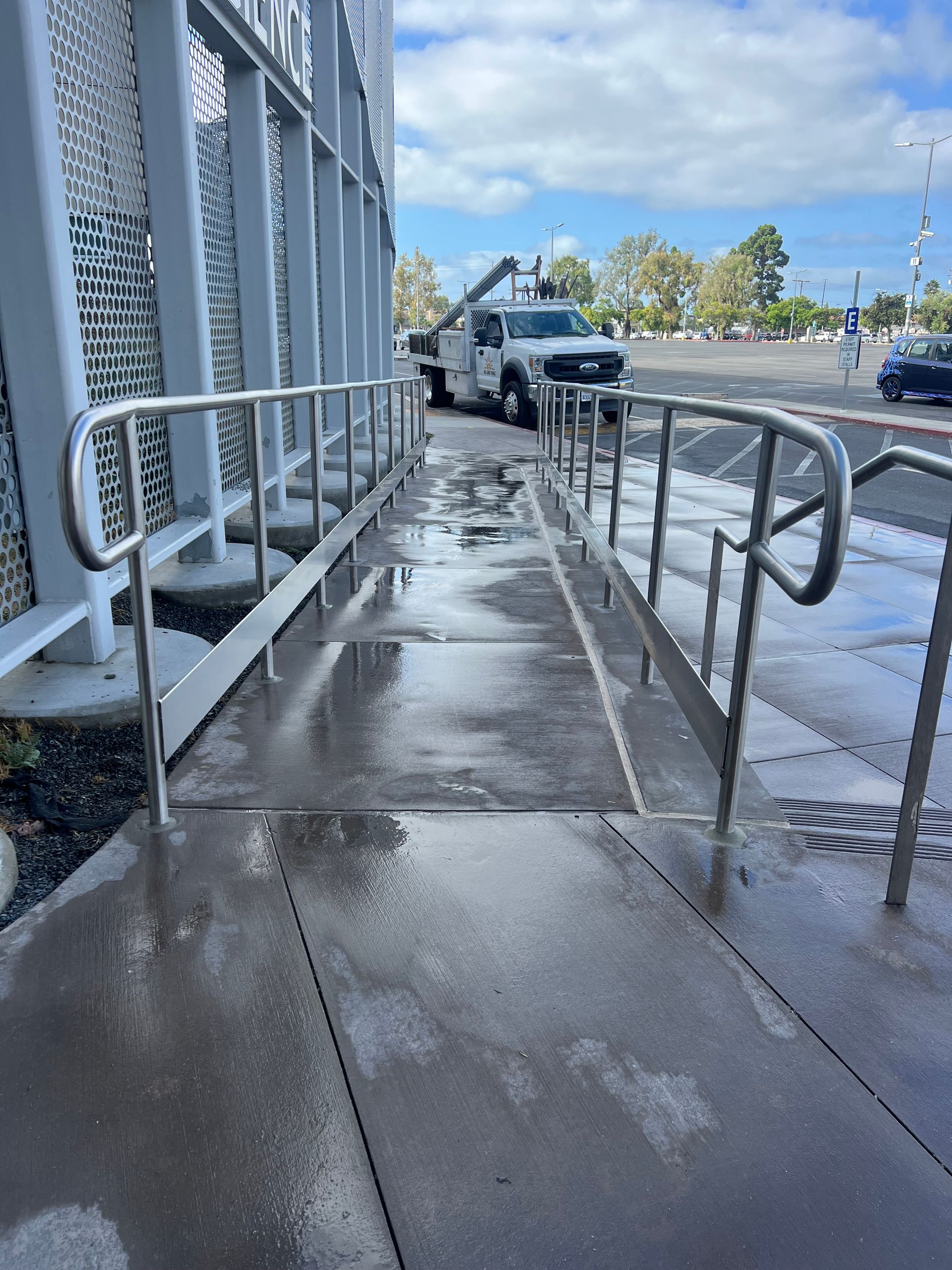 A white truck is parked on the side of the road next to a handicapped ramp.