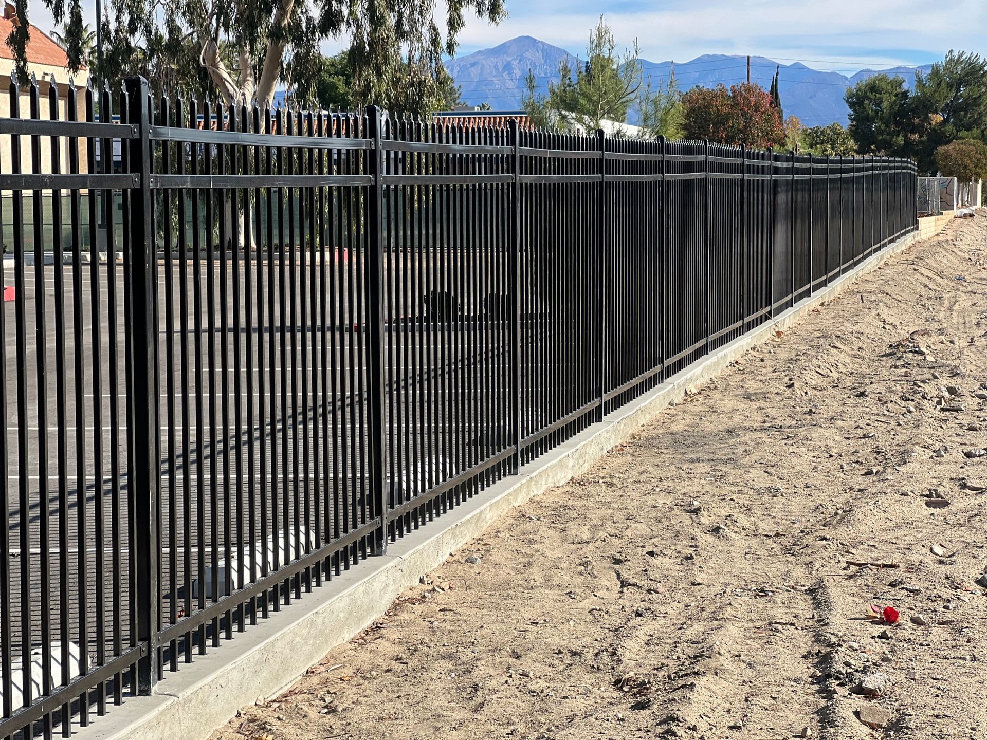 A black metal fence surrounds a dirt field with mountains in the background.