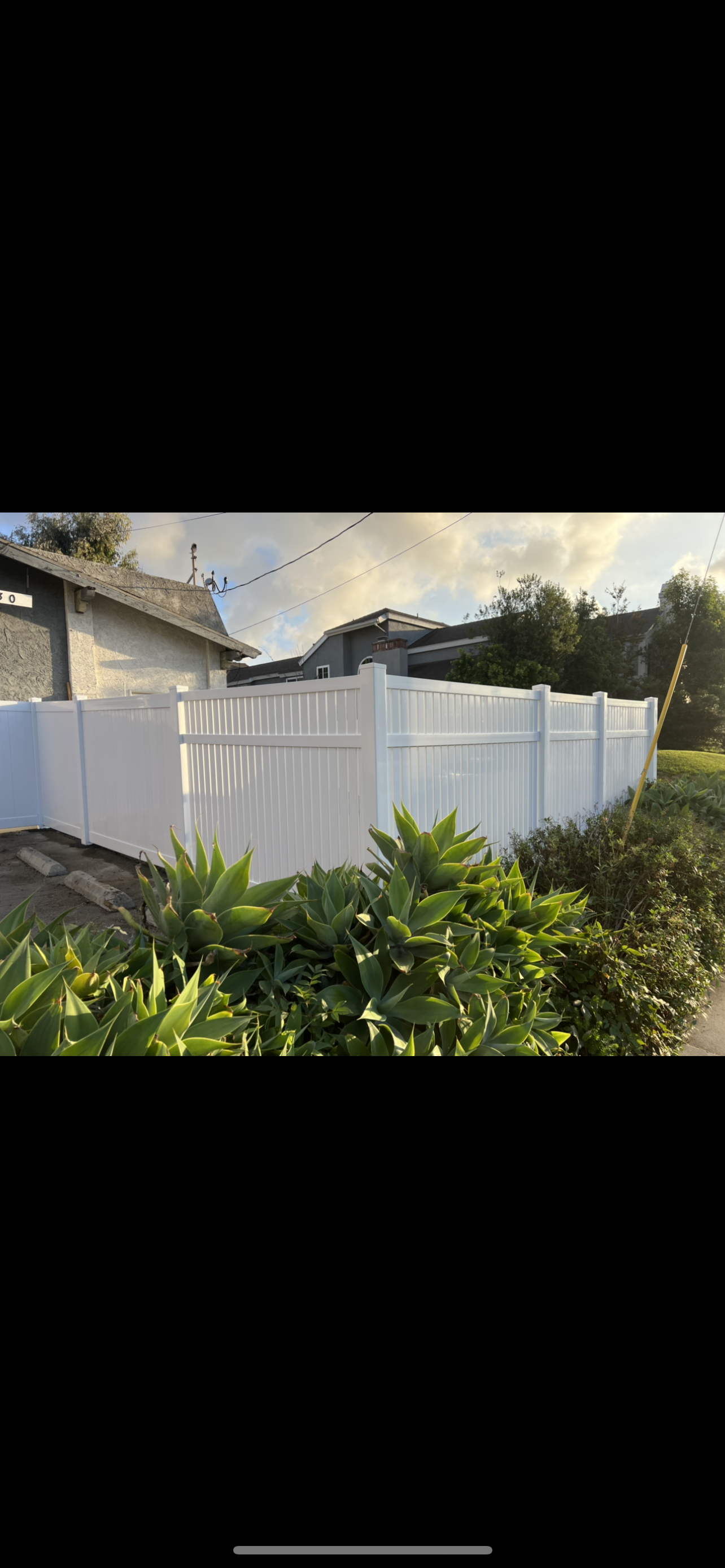 A white fence is surrounded by trees and bushes in front of a house.