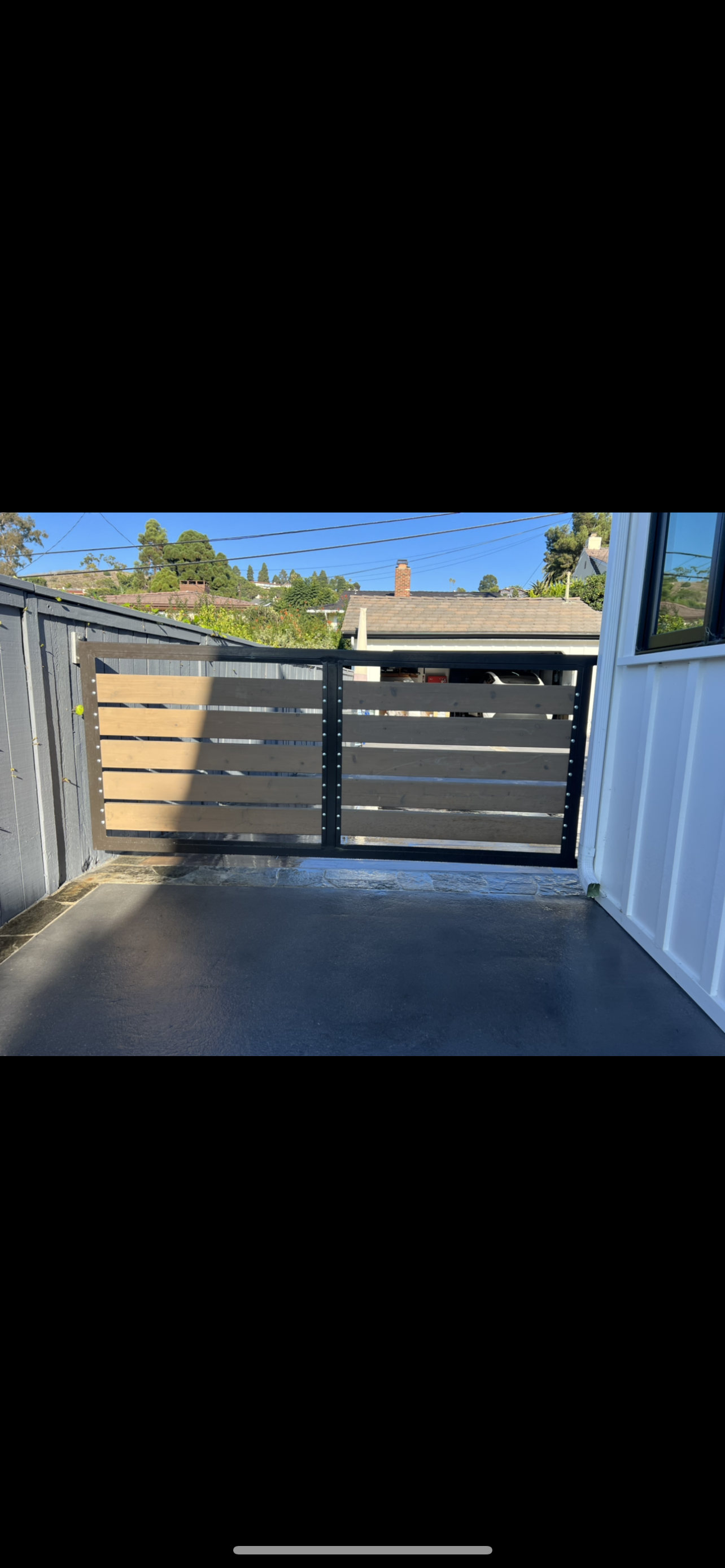 A wooden gate is sitting in the middle of a driveway next to a house.
