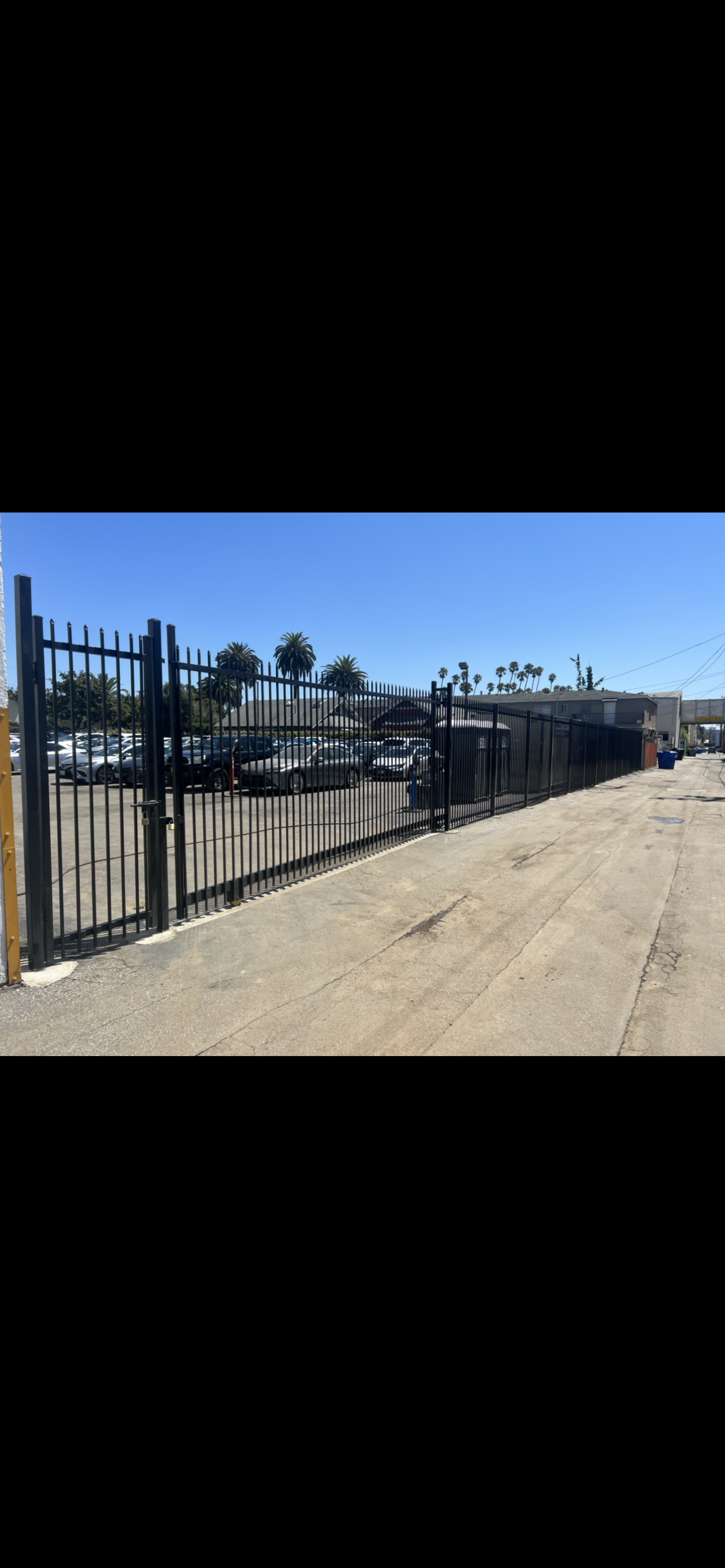 A black metal fence surrounds a parking lot with cars parked in it.