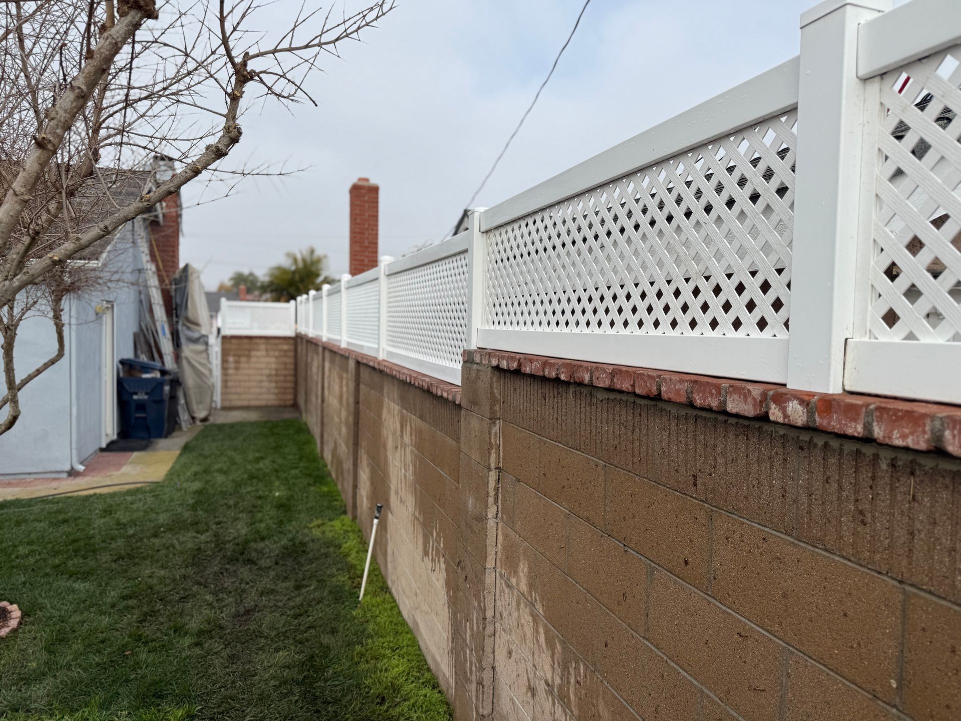 A white lattice fence surrounds a brick wall in a backyard.