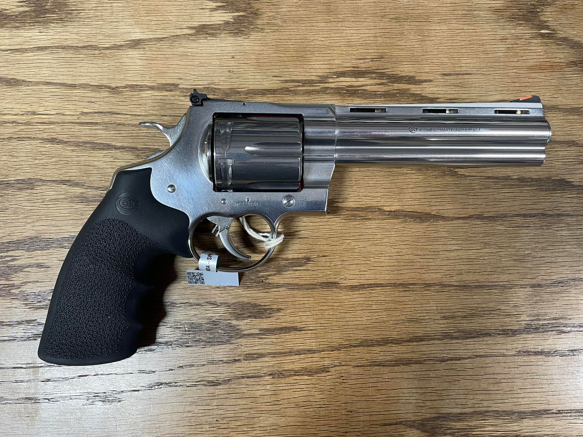A stainless steel revolver with a black grip is sitting on a wooden table.
