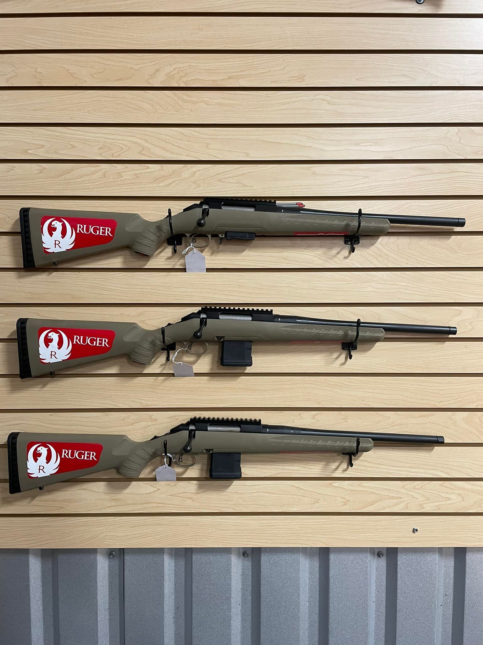 Three sniper rifles are lined up on a wooden wall.