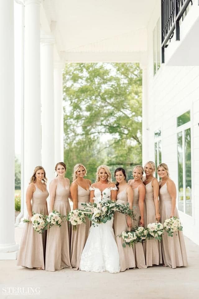 Bride with bridesmaids in blush dresses posing in a white-columned outdoor walkway