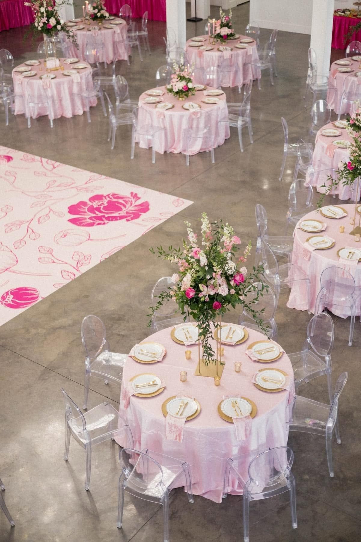Round pink-draped banquet tables with floral centerpieces in a decorated event hall